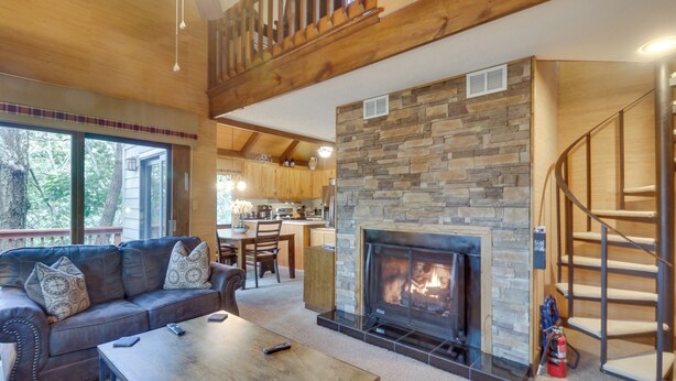 Ein gemütliches Wohnzimmer mit Kamin aus Stein, einer Holztreppe und einem Ledersofa.
