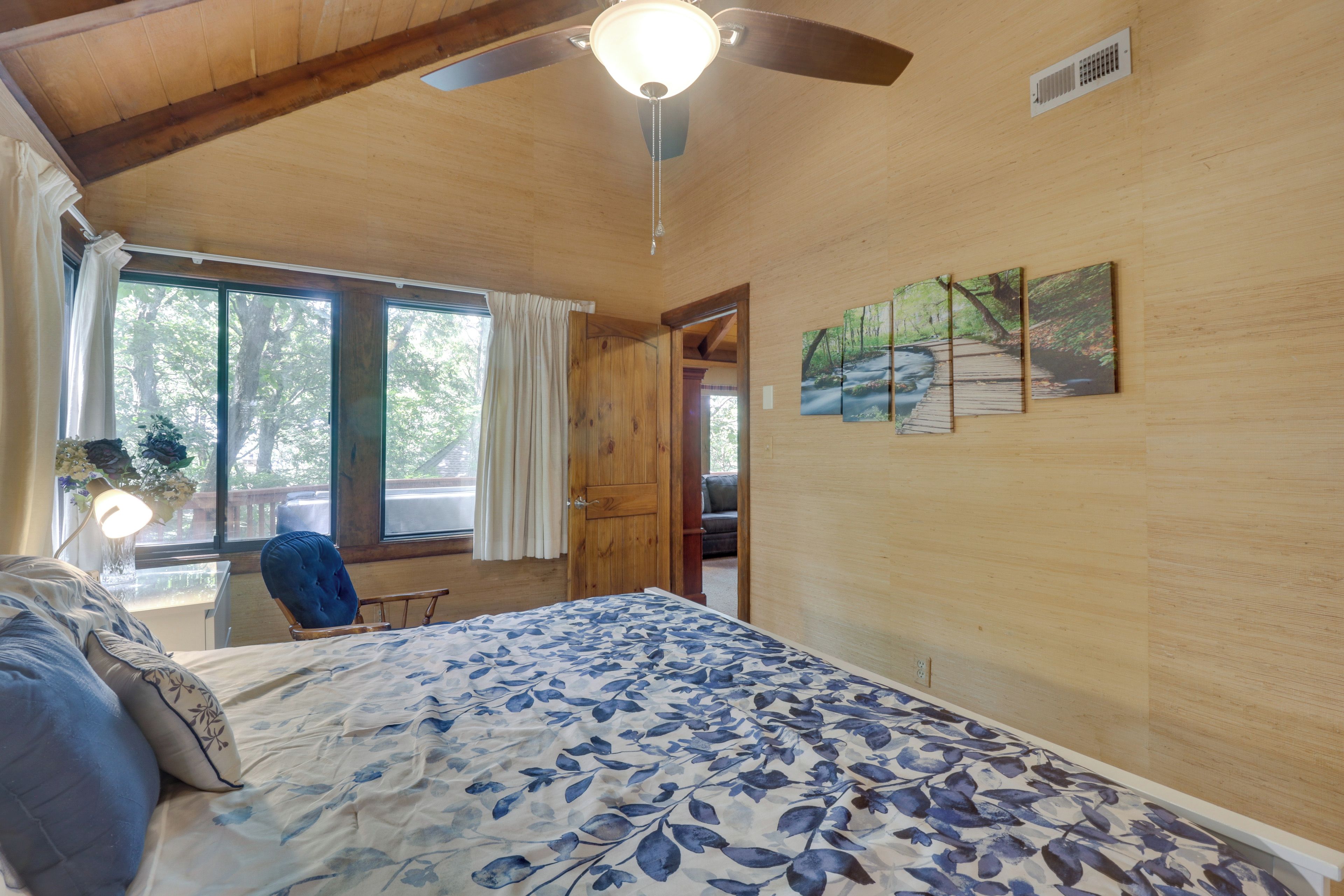 Une chambre avec un plafond en bois, un lit recouvert d’une courtepointe à motifs floraux, une fenêtre avec des rideaux et un tableau accroché au mur.
