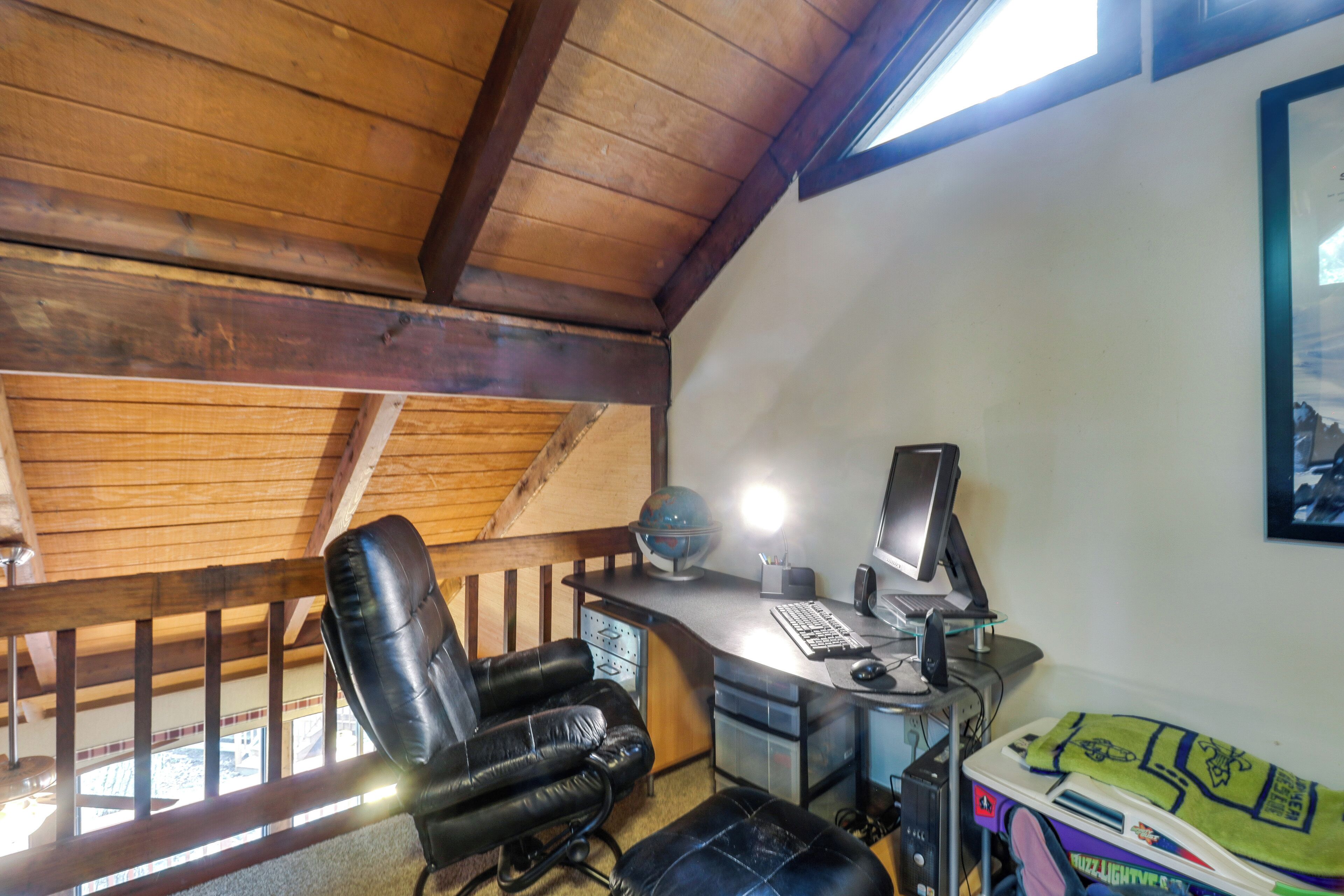 Una habitación con techo de madera, un escritorio con computadora, una silla y una cama con manta.