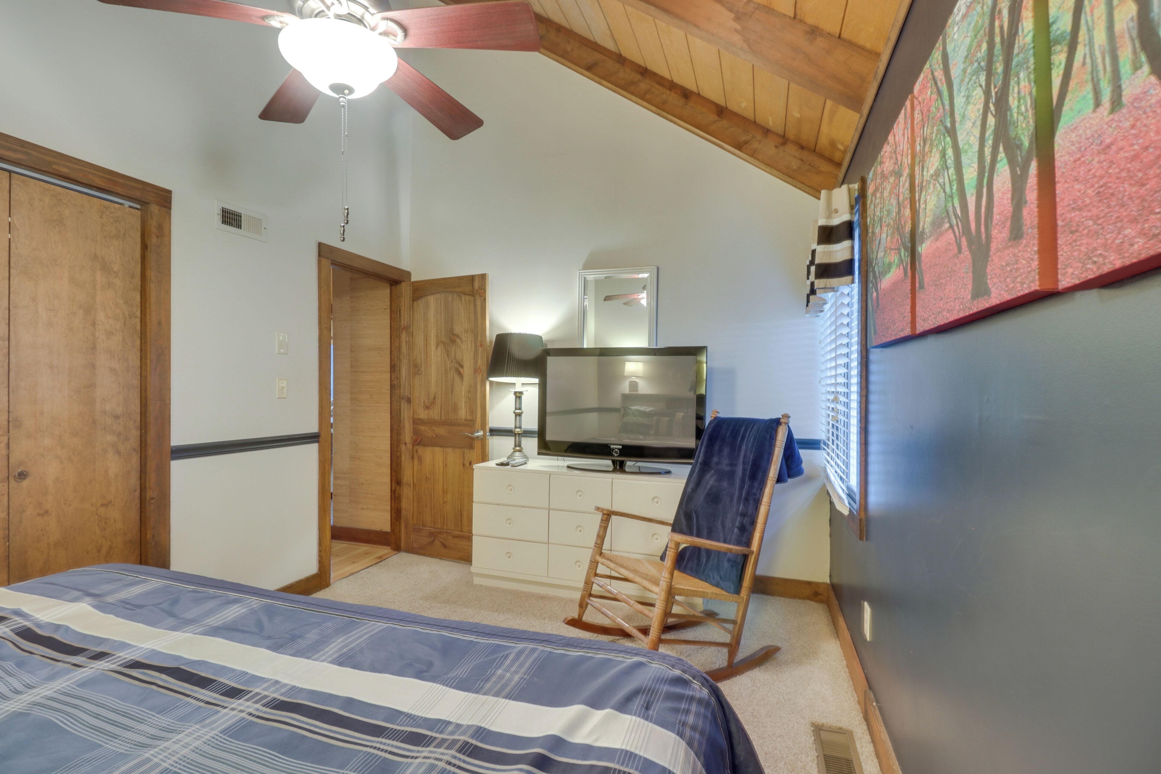 A bedroom with a bed, a television, a rocking chair, and a ceiling fan.