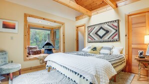 Une chambre confortable avec un grand lit, un coin lecture près de la fenêtre, une cheminée et un plafond en bois.