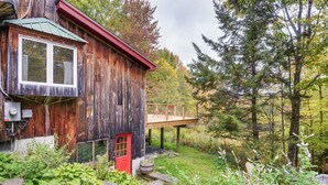 Un chalet rustique en bois, avec une porte rouge, une petite terrasse et un chemin de pierres menant à l’entrée.