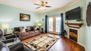 A living room with a fireplace, a ceiling fan, and a large flat-screen TV mounted on the wall. - Steps to Parkway! Pigeon Forge Condo + Pool Access (Pigeon Forge)