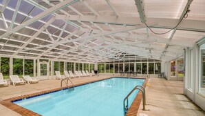 An indoor swimming pool with clear blue water, surrounded by white lounge chairs and a covered roof structure. - Steps to Parkway! Pigeon Forge Condo + Pool Access (Pigeon Forge)