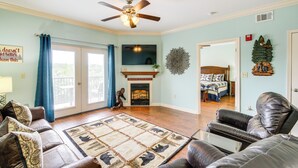 A living room with a fireplace, a ceiling fan, and a view of the bedroom through an open door. - Steps to Parkway! Pigeon Forge Condo + Pool Access (Pigeon Forge)