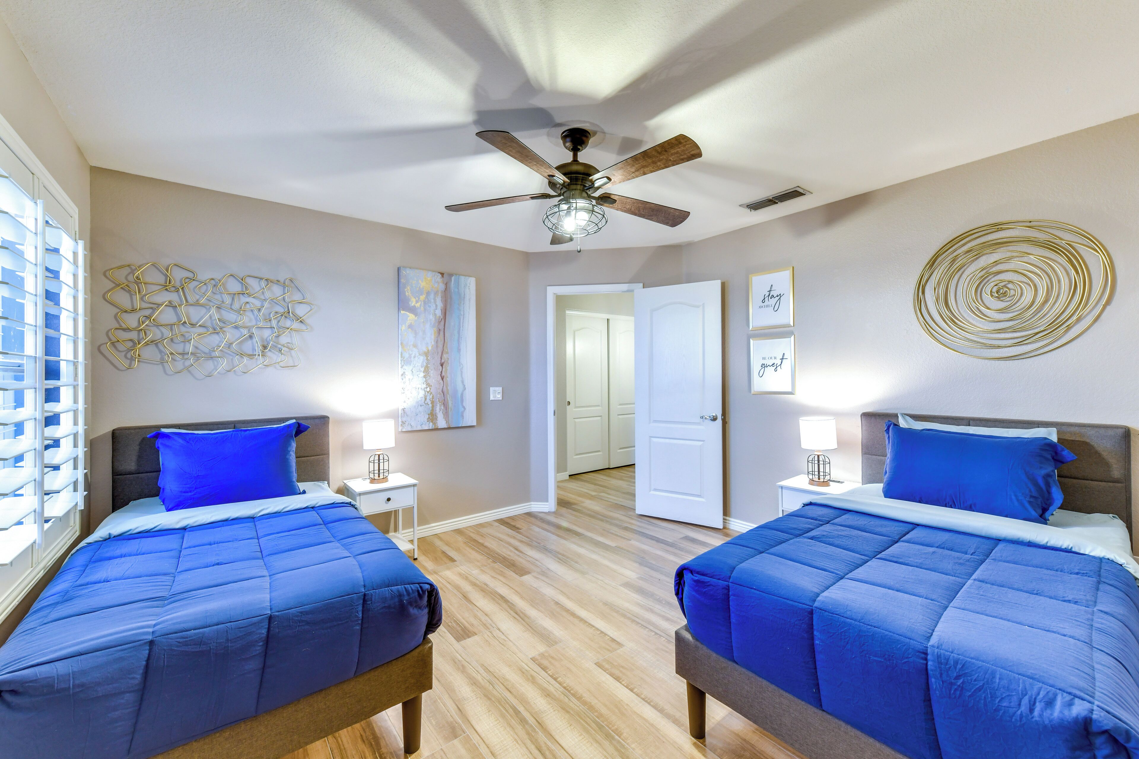 A bedroom with two beds, a ceiling fan, and artwork on the walls.