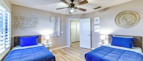 A bedroom with two beds, a ceiling fan, and artwork on the walls.