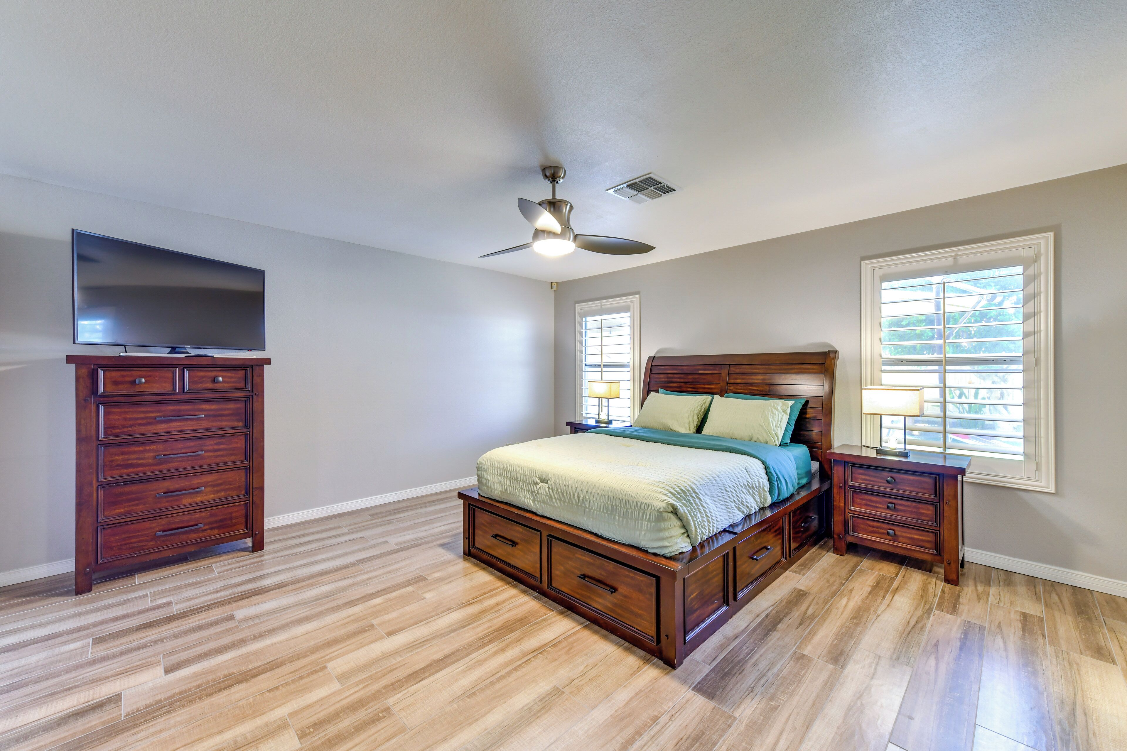 A bedroom with a wooden bed, a nightstand, a dresser, a ceiling fan, and a TV on a stand.