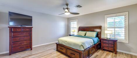 A bedroom with a wooden bed, a nightstand, a dresser, a ceiling fan, and a TV on a stand.