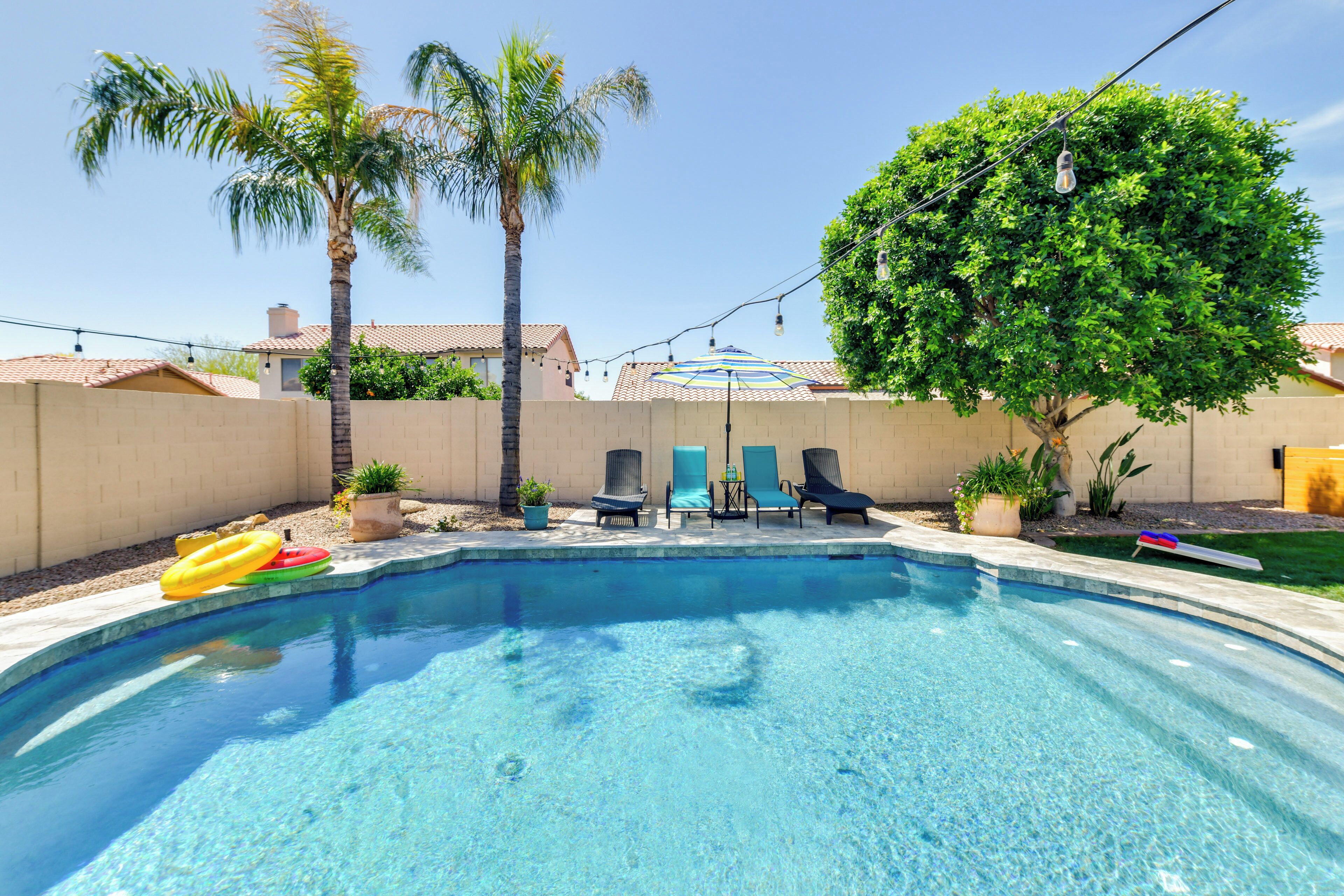 A backyard with a swimming pool, palm trees, and lounge chairs.