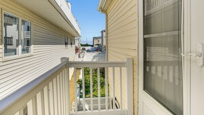 Une rue résidentielle étroite, bordée de maisons des deux côtés, avec un ciel dégagé et un balcon visible, doté d’une balustrade blanche.
