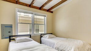 Une chambre avec deux lits, une fenêtre avec des stores et un plafond en bois.