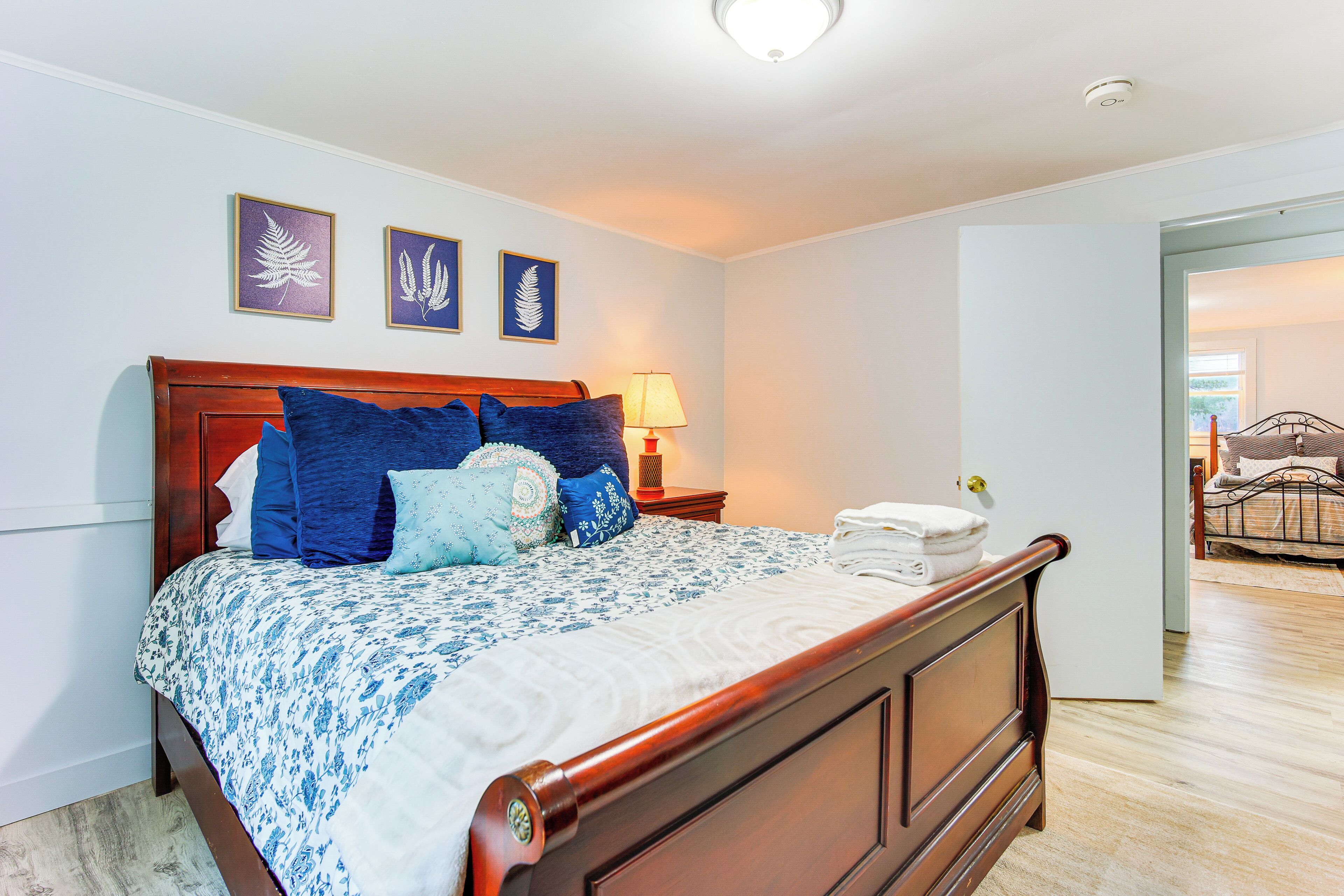 Une chambre à coucher avec un lit en bois, une literie bleue et blanche, et trois décorations murales représentant des feuilles, encadrées.