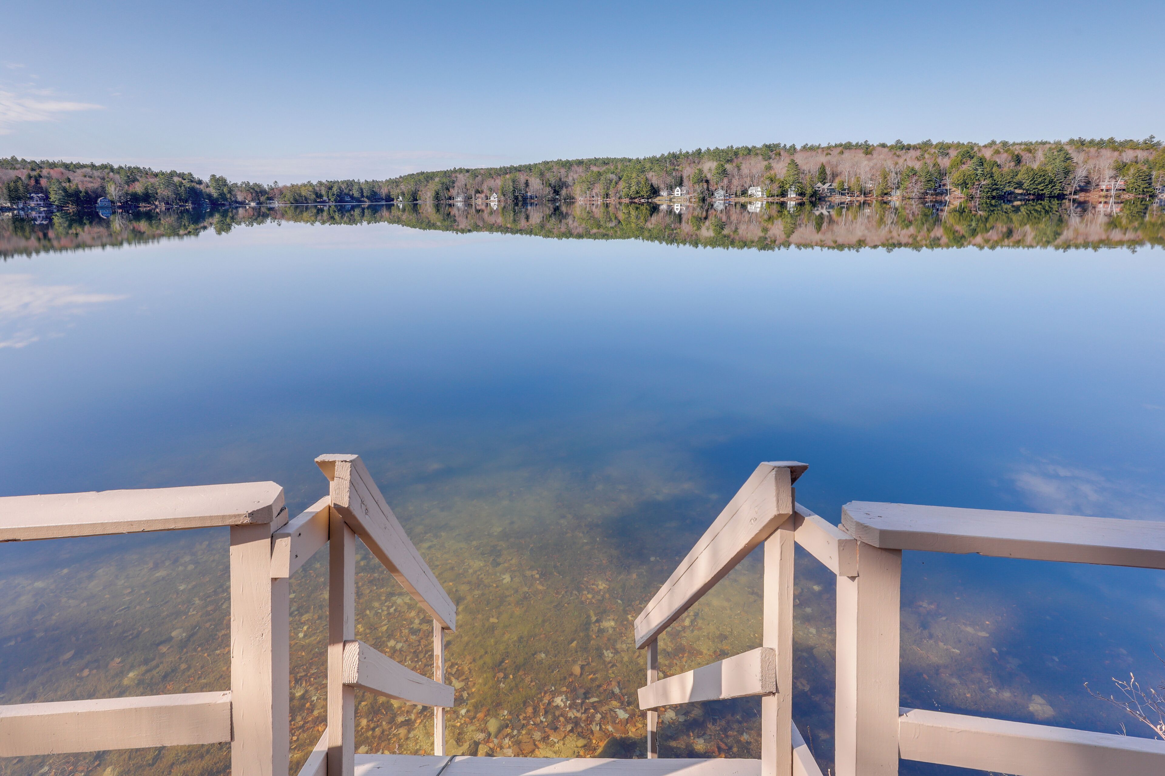 A wooden dock leading into a calm lake with a forested shoreline in the background.