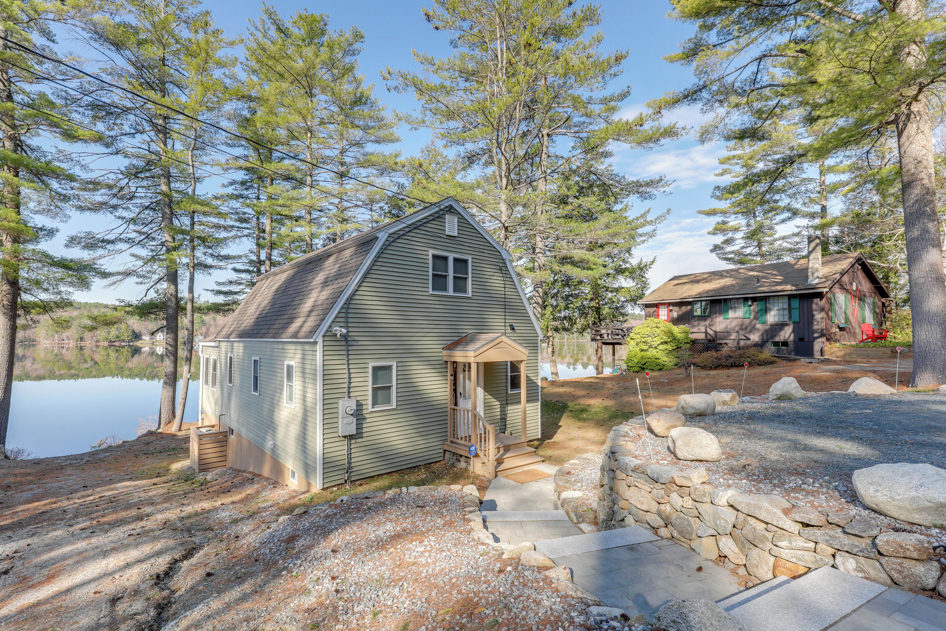 A small cabin with a porch, a stone wall, and a gravel path leading to the entrance.