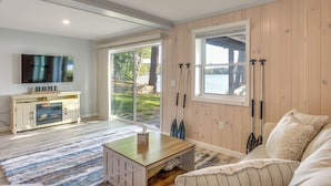 A modern living room with a fireplace, a television, and a view of the outdoors. - Lakefront Cabin w/ Panoramic Water View & Access (Sunapee)