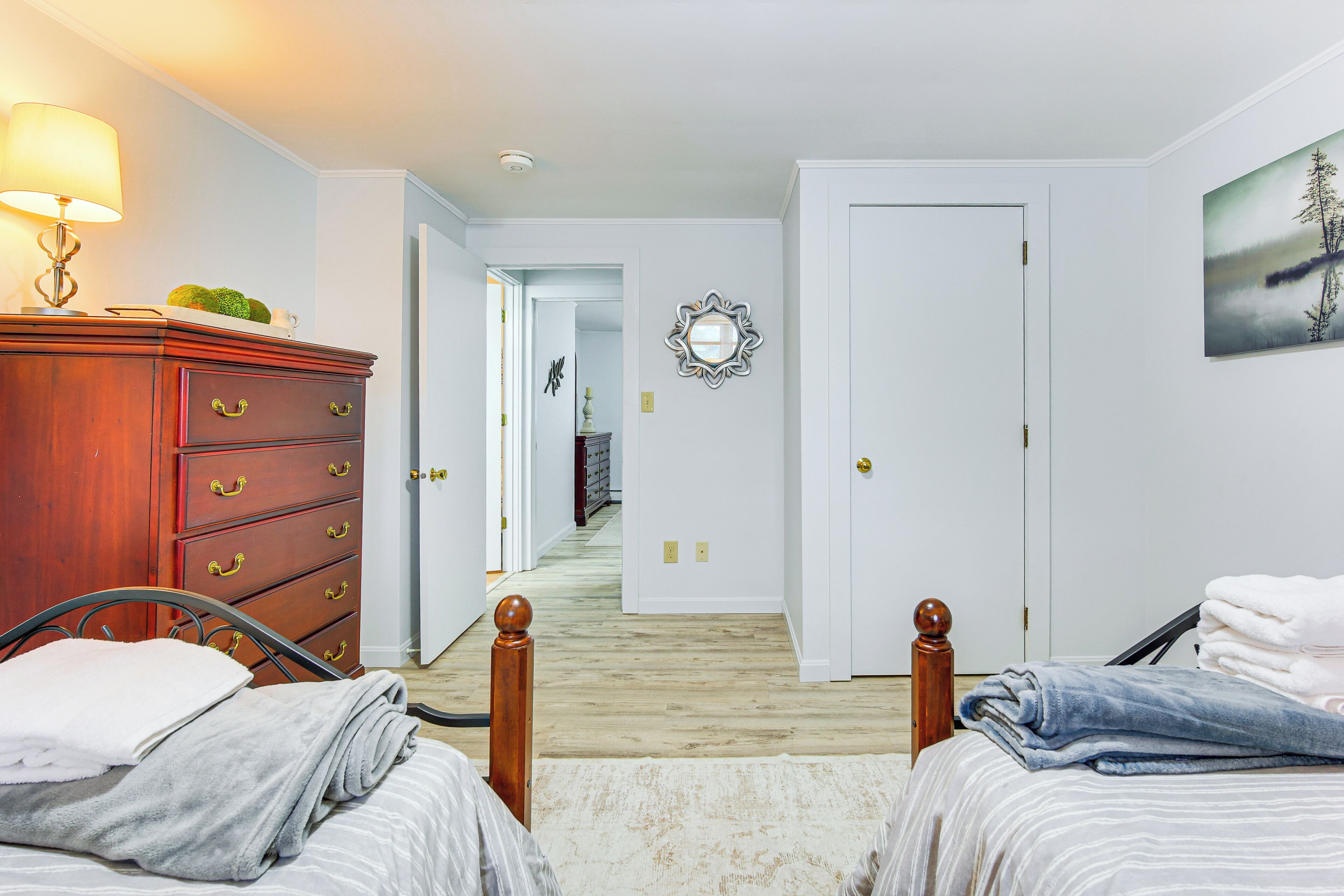 A bedroom with two beds, a dresser, a lamp, and a painting on the wall.