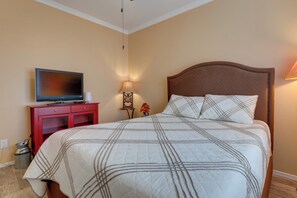 Un lit bien fait, recouvert d’une couverture à carreaux, un téléviseur posé sur un meuble rouge et une lampe fixée au mur.
