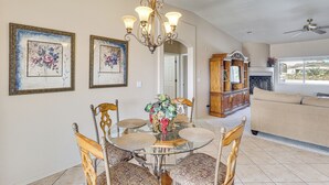 Un coin repas avec une table en verre entourée de chaises, un lustre et deux tableaux représentant des motifs floraux, accrochés au mur.