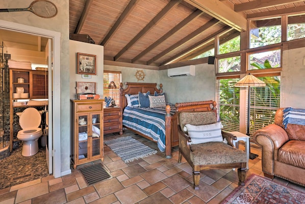 A spacious room with a large bed, a wooden chair, a leather sofa, and a bathroom with a toilet and sink.