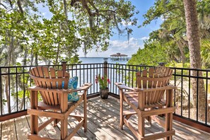 A wooden deck with Adirondack chairs and a potted plant, overlooking a body of water and a gazebo.