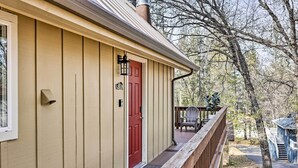 A wooden house with a red door, a porch with a railing, and a view of trees and a blue structure in the background. - California Cabin w/ Lake Access: 28 Mi to Yosemite (Groveland)