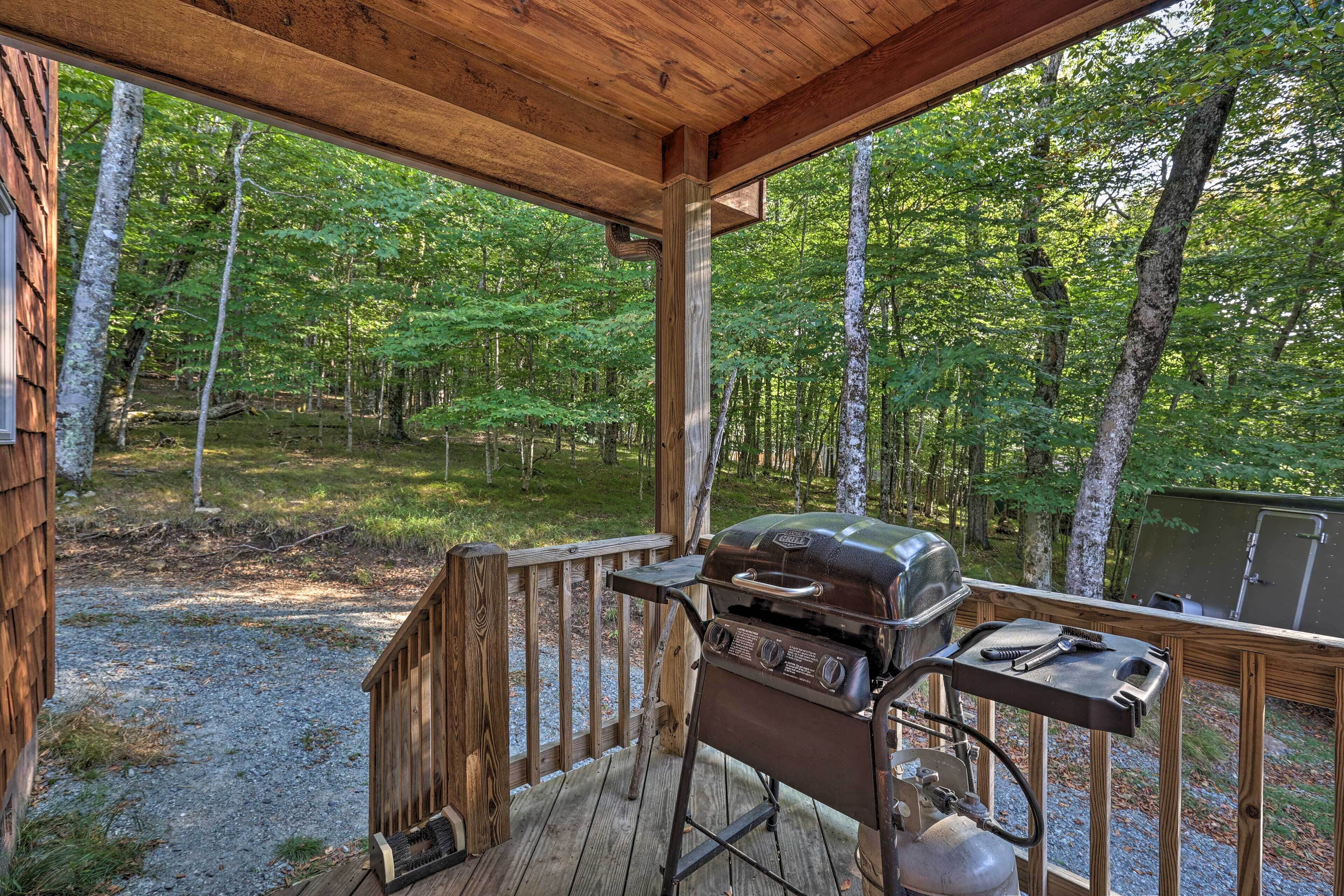 A covered outdoor area with a grill and a gas tank, surrounded by a wooden deck and forest.