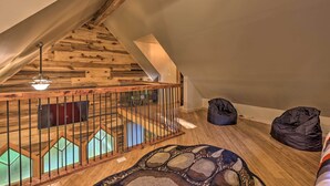 Um quarto estilo loft com teto de madeira, escada com guarda-corpo de madeira e dois sacos de feijão no chão.