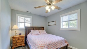 Une chambre à coucher avec un lit en bois, une table de chevet avec une lampe et deux fenêtres équipées de stores.
