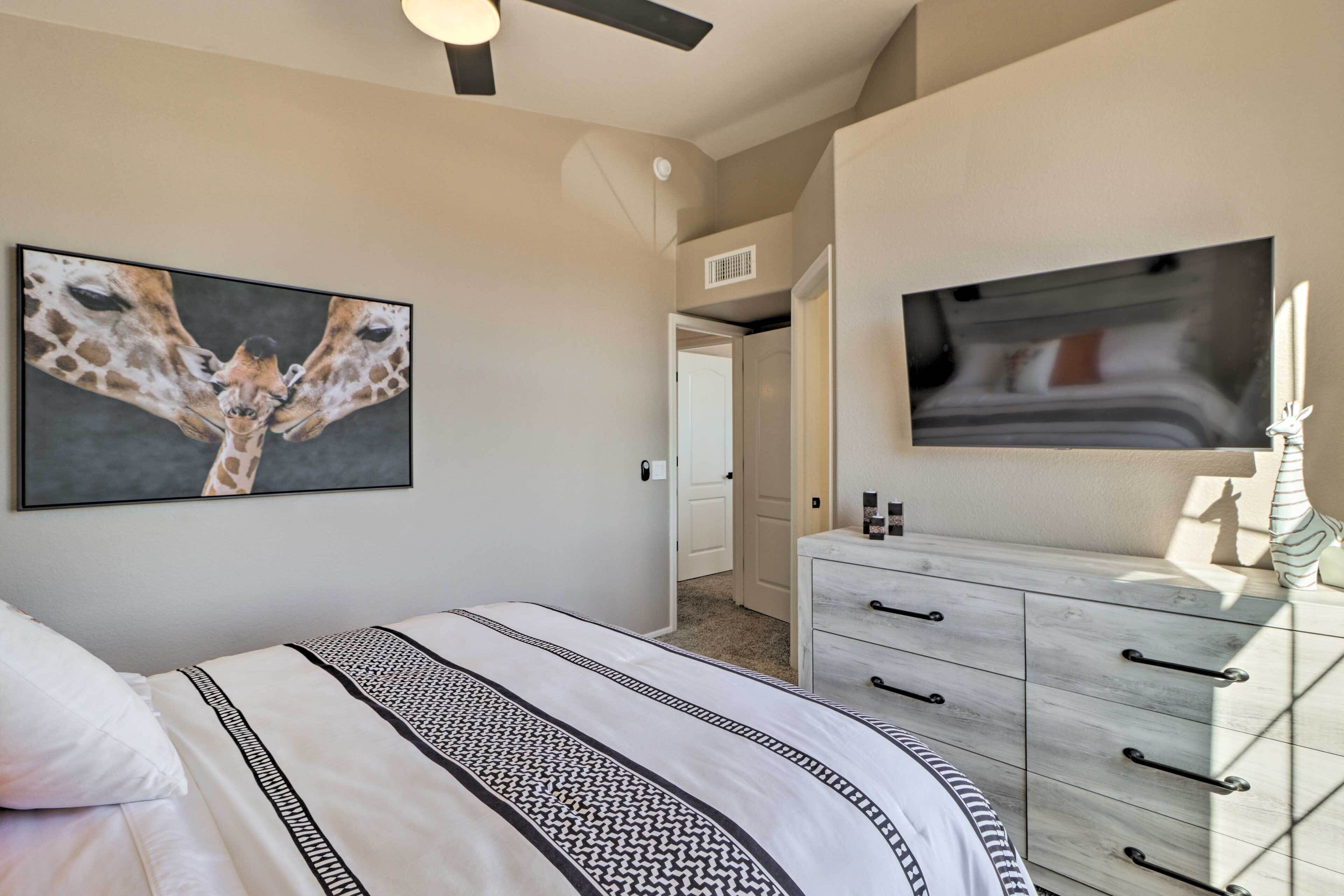 A bedroom with a bed, a dresser, a television, and a giraffe painting on the wall.
