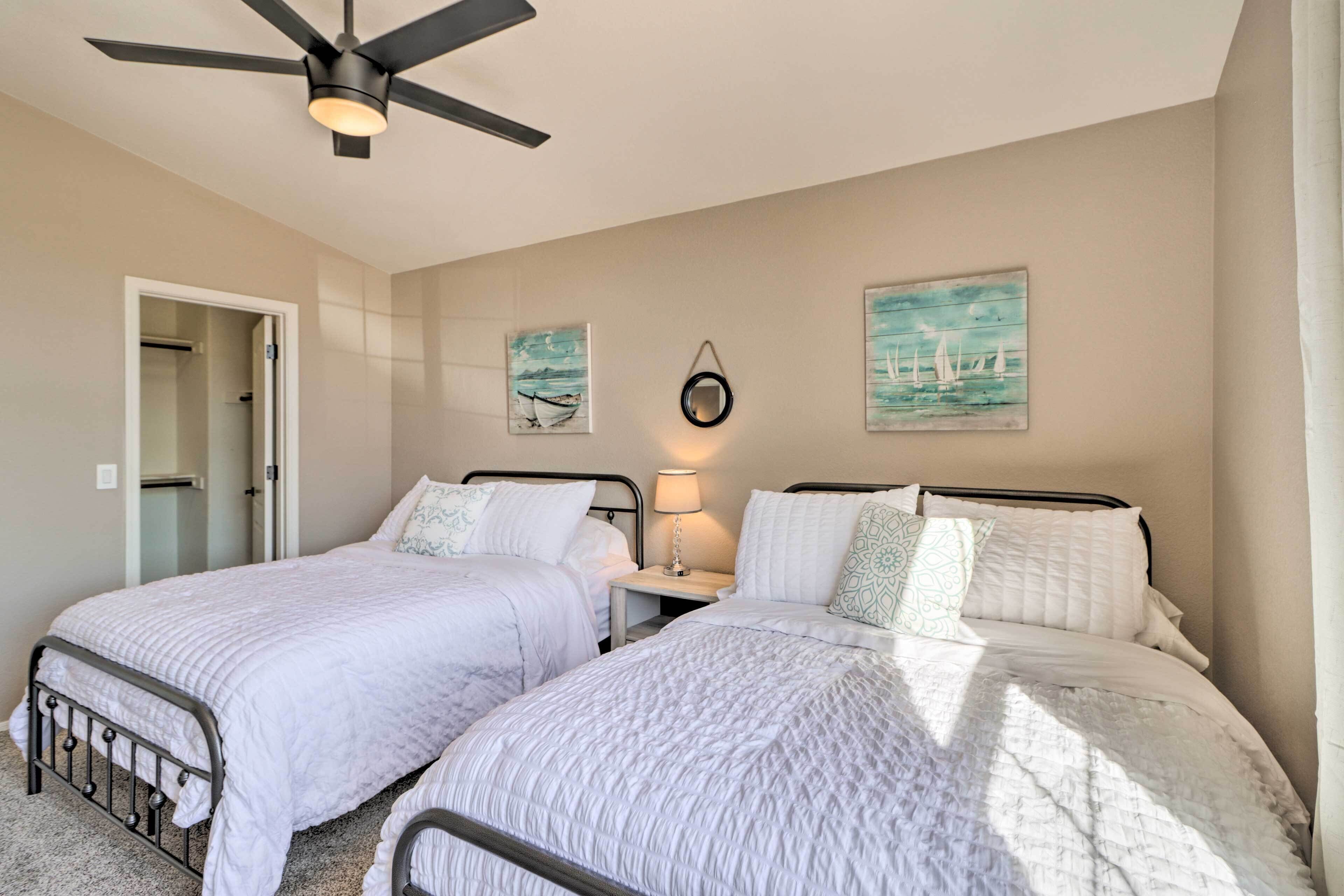 A bedroom with two beds, a ceiling fan, and artwork on the walls.