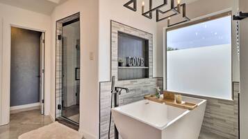 Un baño moderno con una bañera independiente, un box de ducha con mampara de vidrio y un ventanal con vistas al cielo.
