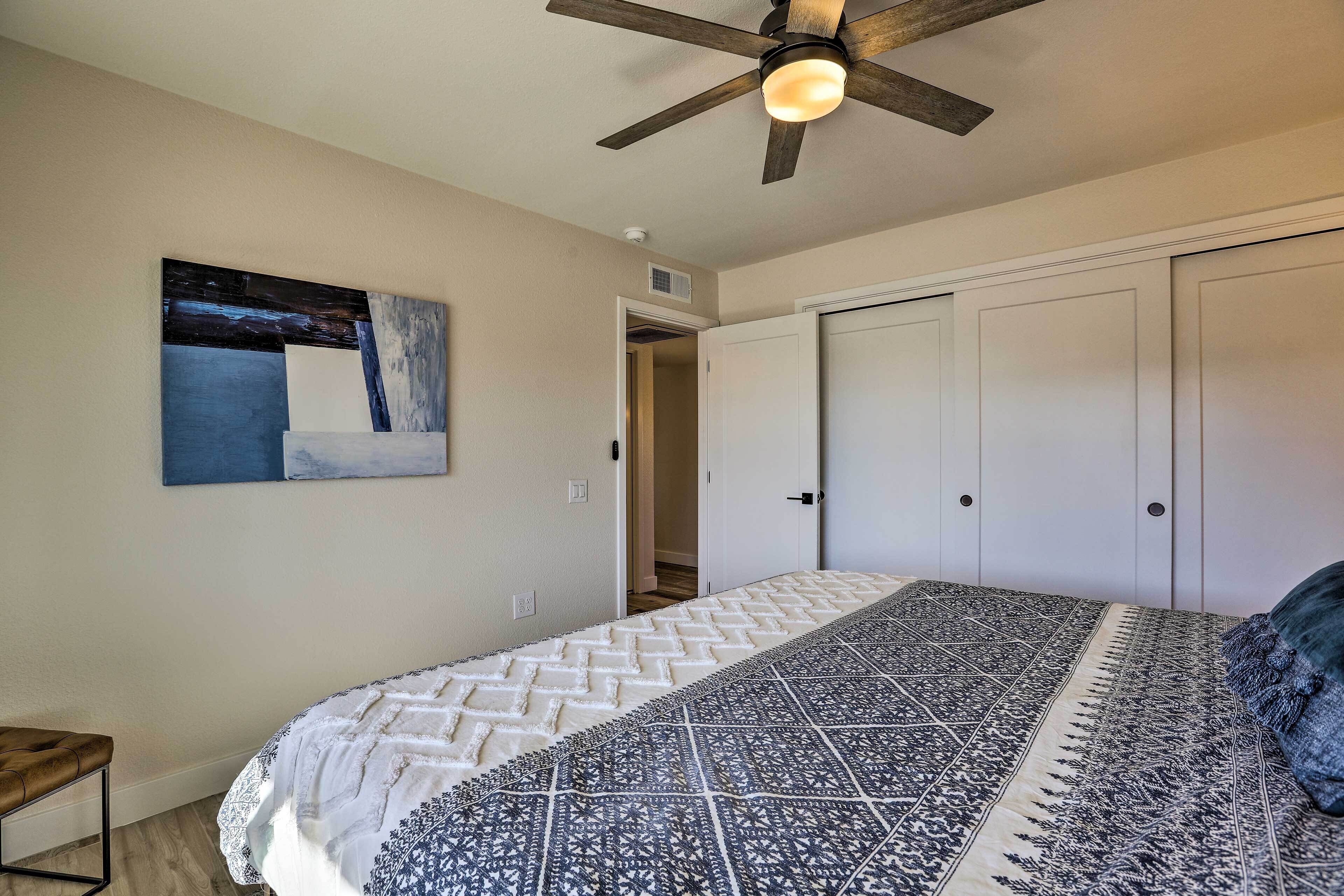 A bedroom with a bed, a ceiling fan, a door, and a painting on the wall.