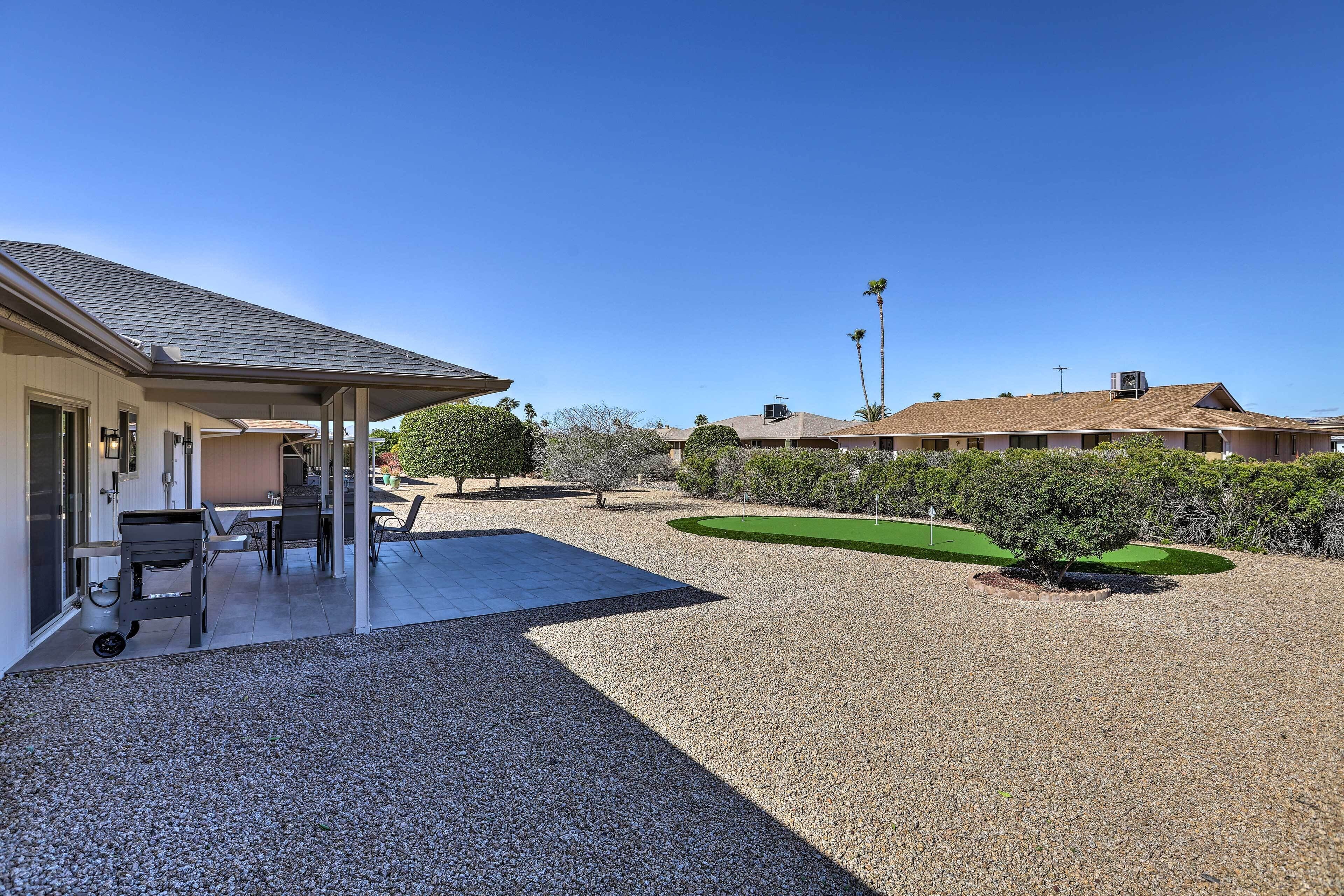 A residential property with a covered patio, a small lawn, and a gravel driveway.