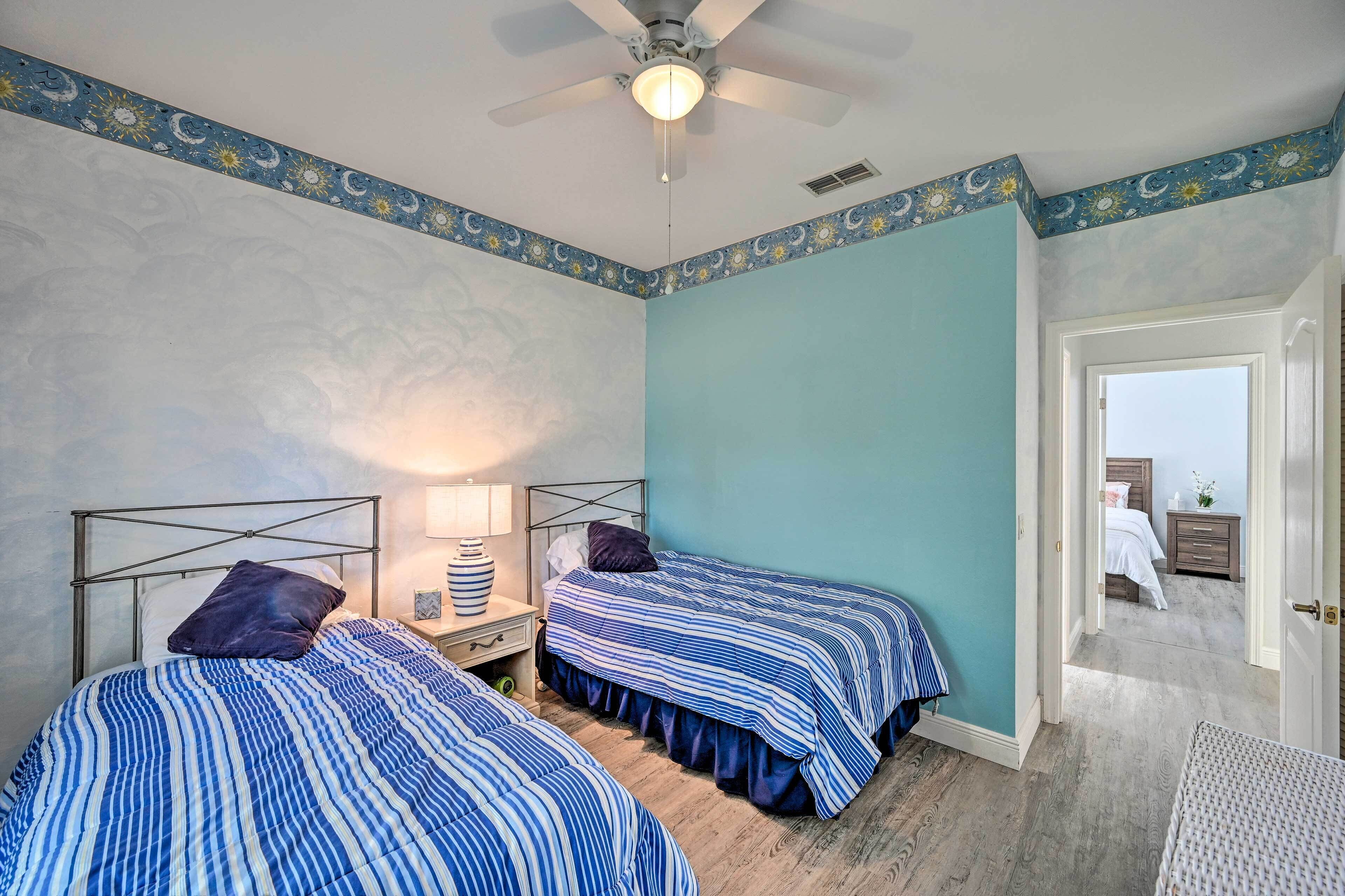 A bedroom with two beds, a ceiling fan, and a door leading to another room.