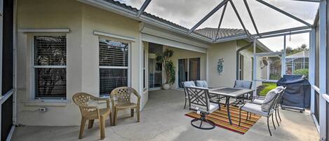 A covered patio with a table and chairs, a grill, and a view of the house.