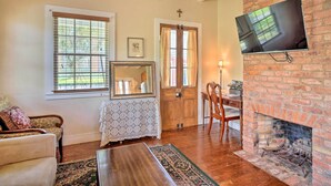 A cozy living room with a fireplace, wooden furniture, a television mounted on the wall, and large windows. - Idyllic Houma Vacation Rental on Shared Pond! (Houma)