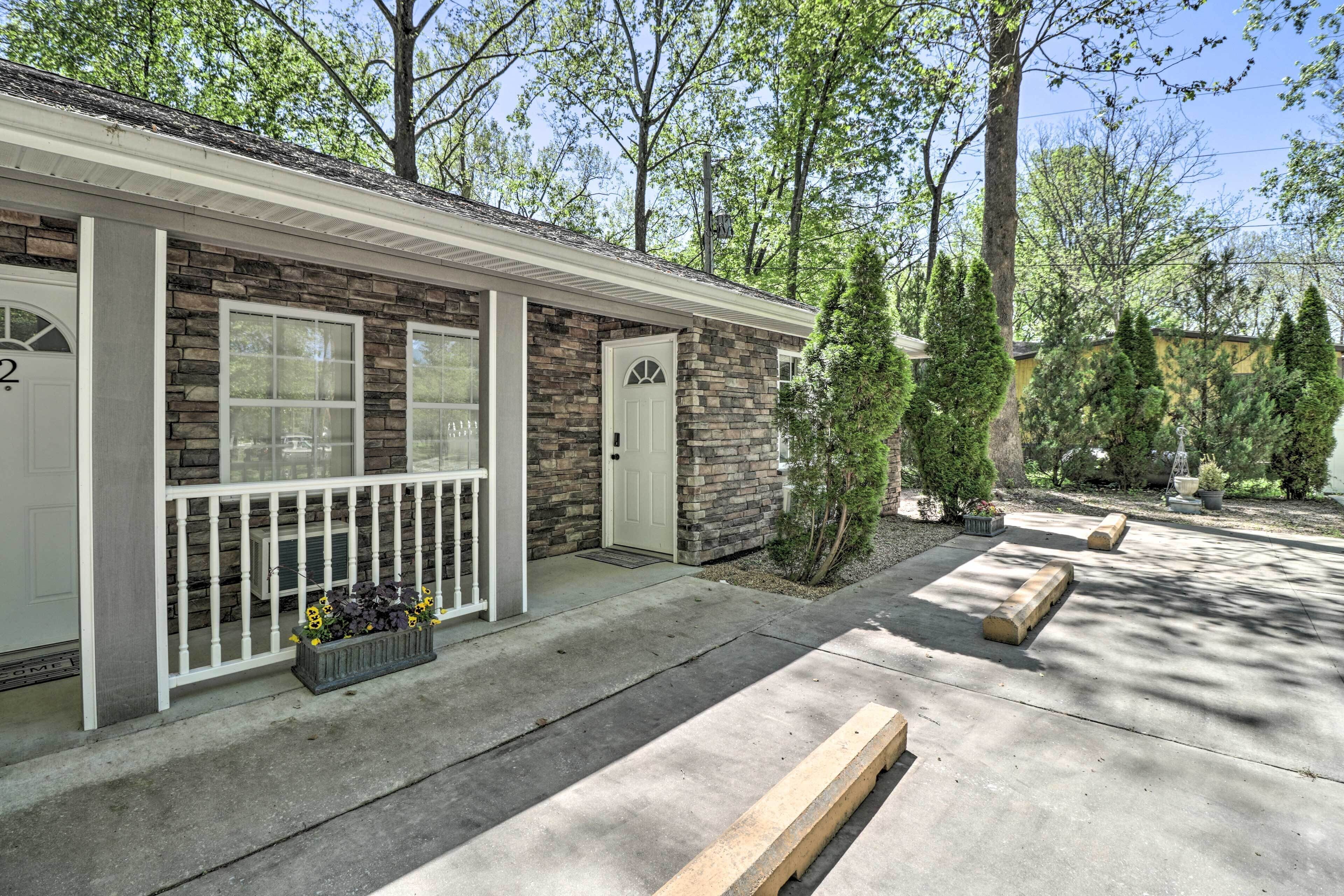 A two-story stone building with a white front door and windows, a covered porch, and a concrete driveway.