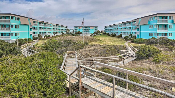 A beachfront hotel with multiple blue buildings, wooden boardwalks, and a flagpole. - Beachfront Condo w/ Boardwalk & Pool Access! (Atlantic Beach)