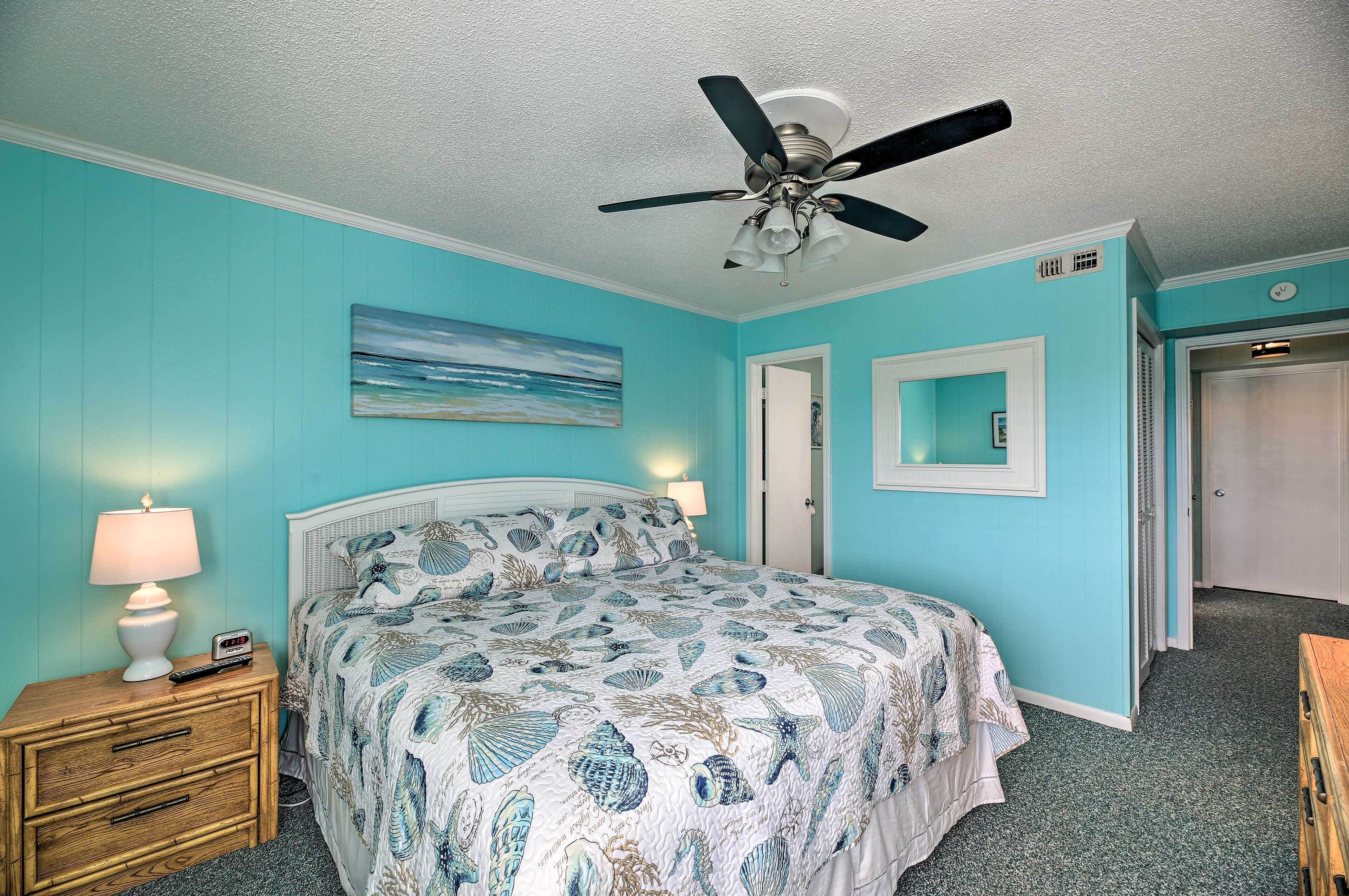 A bedroom with a bed, nightstand, lamp, ceiling fan, and a door.