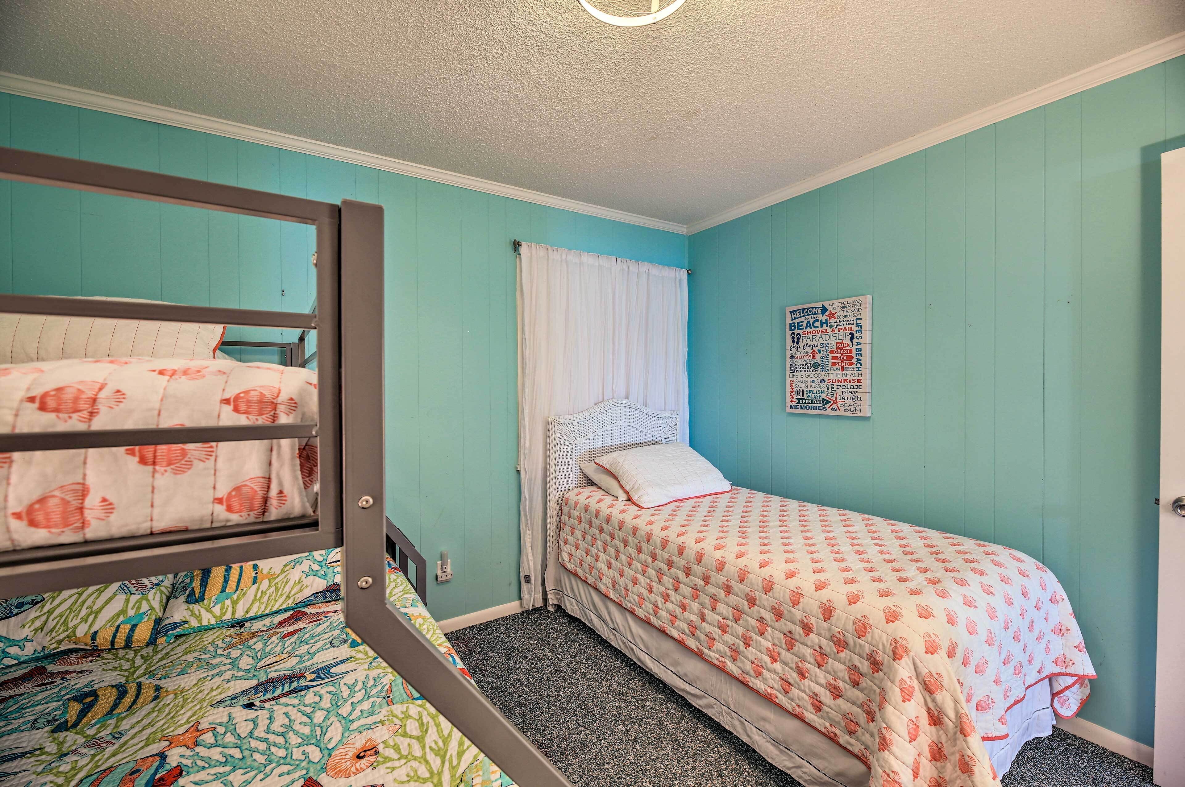 A room with a bunk bed, a single bed, and a poster on the wall.