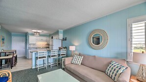 A living room with a beige sofa, a coffee table, and a dining area with chairs and a table. - Beachfront Condo w/ Boardwalk & Pool Access! (Atlantic Beach)