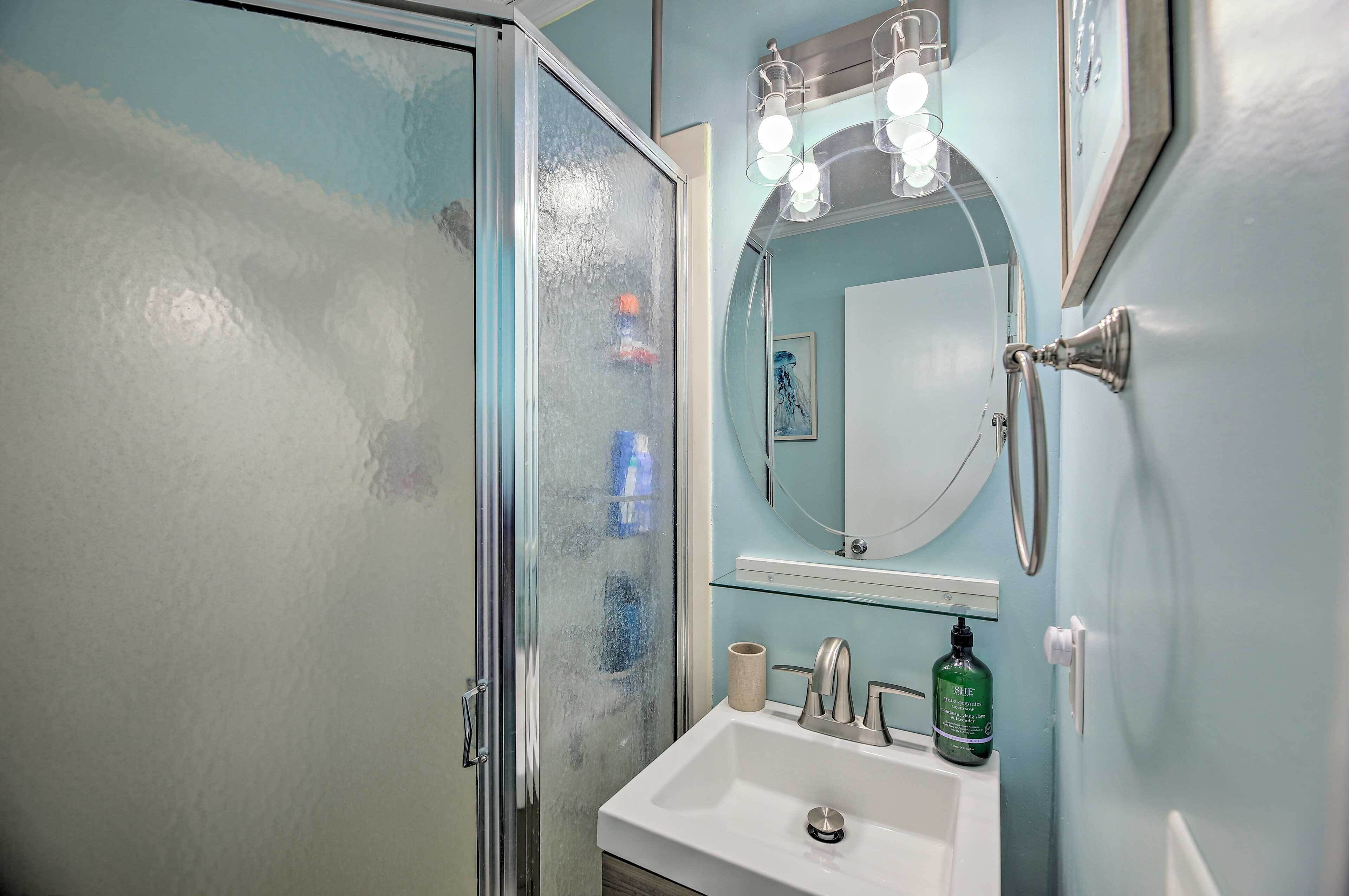 A bathroom with a glass shower enclosure, a sink with a mirror above it, and a towel rack.