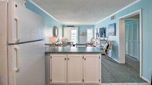 A kitchen with white cabinets, a refrigerator, and a blue accent wall. - Beachfront Condo w/ Boardwalk & Pool Access! (Atlantic Beach)