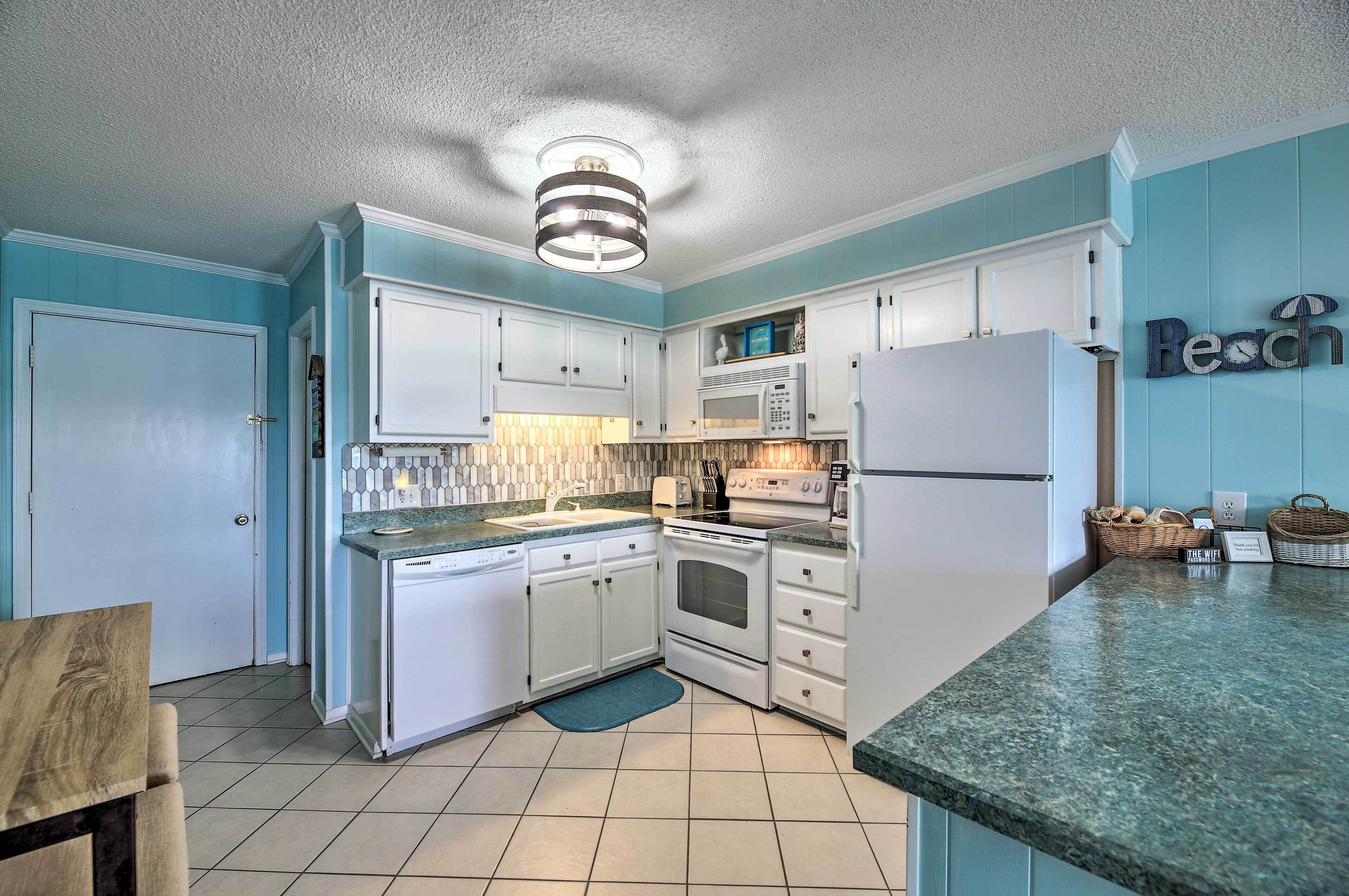 A kitchen with white cabinets, a microwave, a stove, and a refrigerator. There is a blue wall with a sign that reads "Beach".