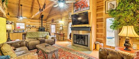 A cozy log cabin interior with leather sofas, a fireplace, a television, and wooden walls.