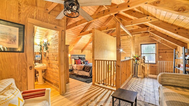 A cozy wooden cabin interior with a loft bedroom, a balcony, and a living area with a sofa and a small table. - Quiet Cabin Retreat on 30 Acres Near Kentucky Lake (New Concord)