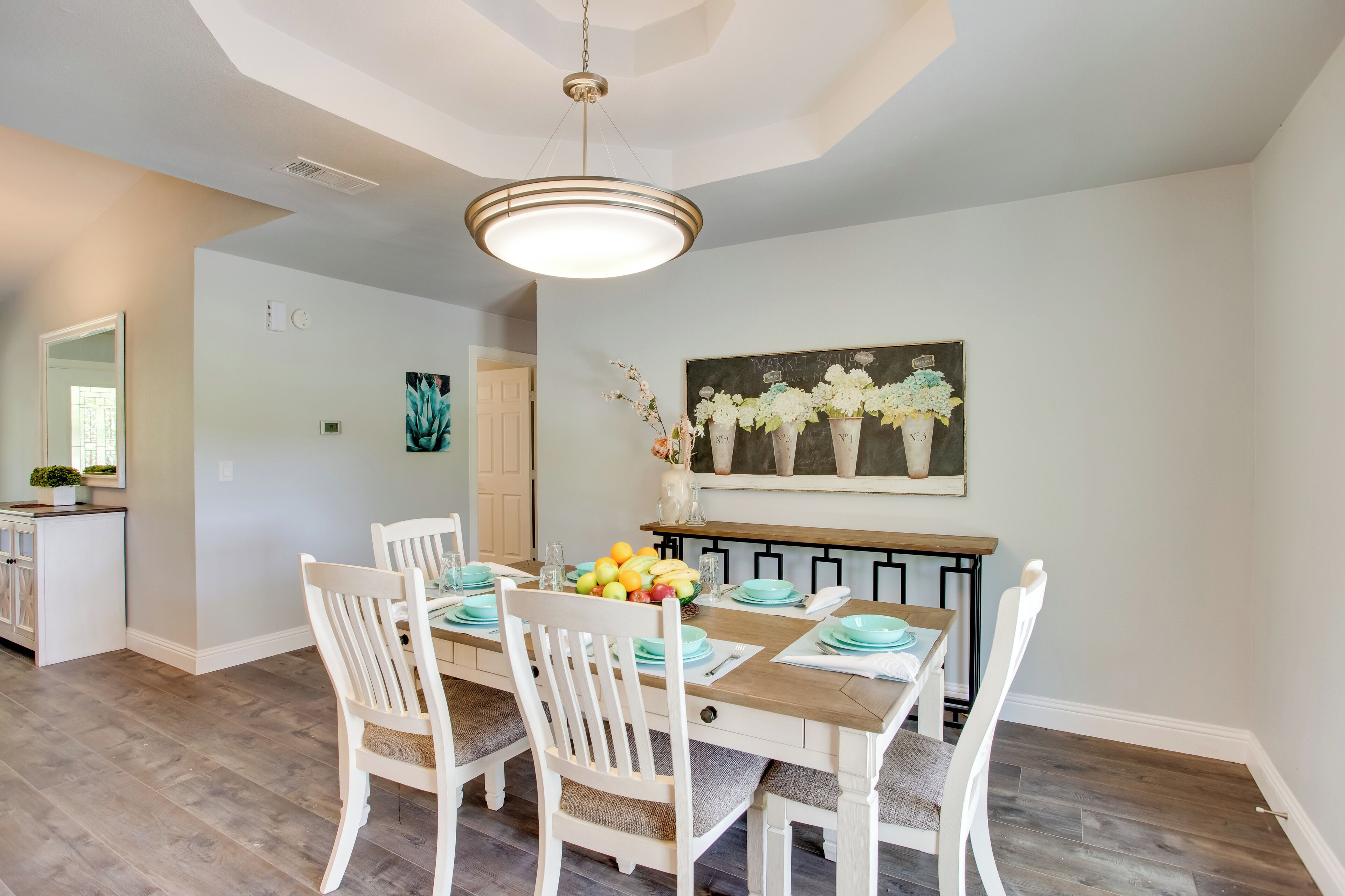 A dining area with a wooden table set for four, white chairs, and a fruit bowl on the table.