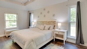 Une chambre à coucher avec un lit, des tables de chevet, un ventilateur de plafond et une fenêtre avec des rideaux.