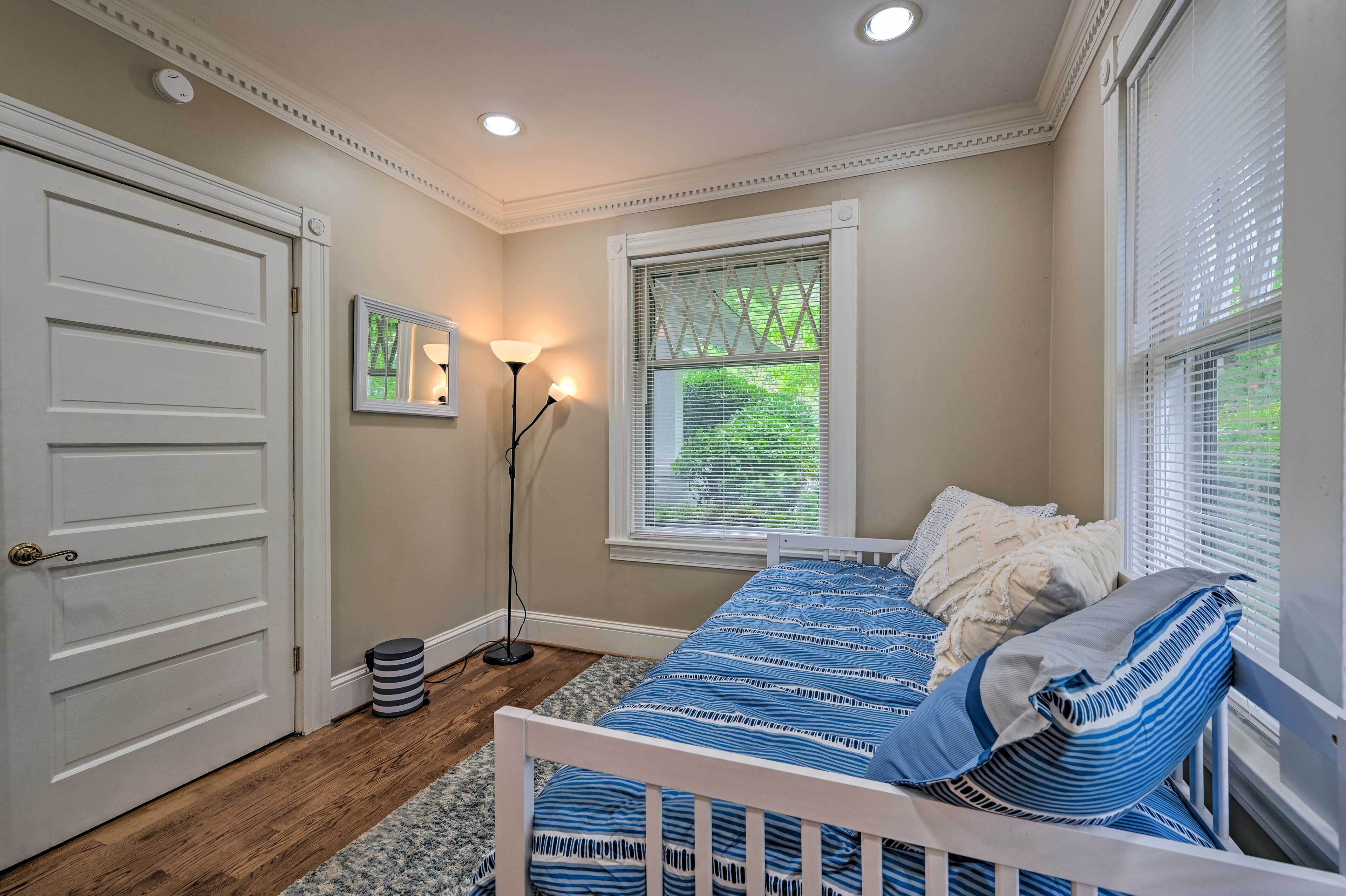 A bedroom with a white bed, a window with blinds, a floor lamp, and a door.